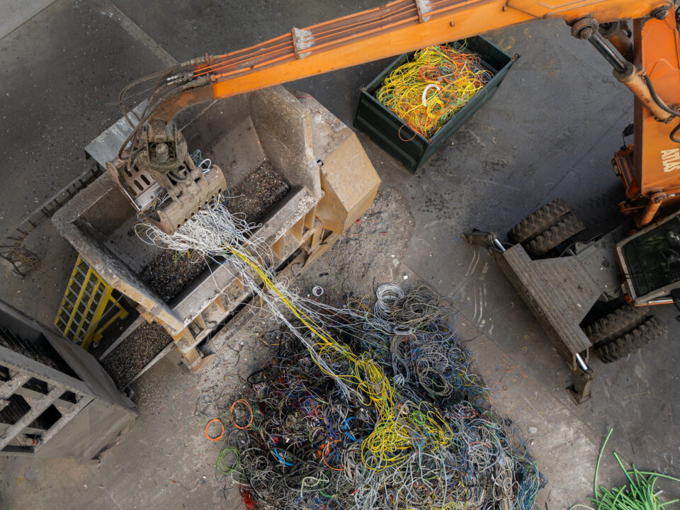 Luchtfoto van kabelverwerking bij Kopuur: overslagkraan voert gemengd kabelafval in de voorbreker, eerste stap in het koperrecyclageproces